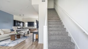 A modern living room with a sofa, coffee table, and a kitchen in the background. - Landing | Spectacular 3BD in Lee's Summit (Lee's Summit)