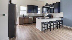 A modern kitchen with dark cabinets, a stainless steel refrigerator, a dishwasher, a microwave, and a large island with bar stools. - Landing | Incredible 3BD in Lee's Summit (Lee's Summit)