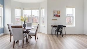 A spacious room with a dining table and chairs, a desk with a chair, large windows, and a painting on the wall. - Landing | Incredible 3BD in Lee's Summit (Lee's Summit)