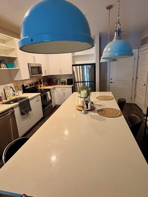 A modern kitchen with white cabinets, stainless steel appliances, and a central island with a blue pendant light.
