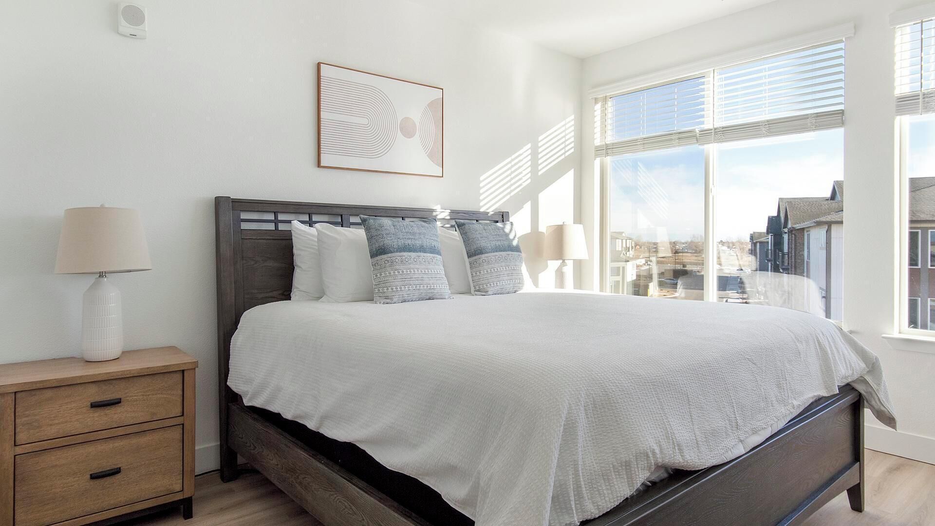 Camera da letto con un grande letto, un comodino, una lampada e una finestra con vista sulla città.