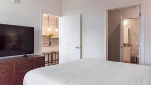 A bedroom with a large bed, a TV on a wooden dresser, and a door leading to a bathroom. - Landing | Spectacular 1BD, Gym, Clubhouse (Longmont)