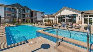 Piscina com espreguiçadeiras e guarda-sóis, cercada por edifícios de apartamentos.