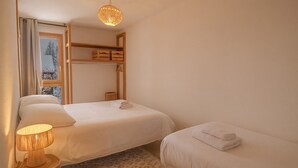 Un dormitorio con dos camas, un estante de madera, una lámpara y vistas a un paisaje nevado a través de una ventana.