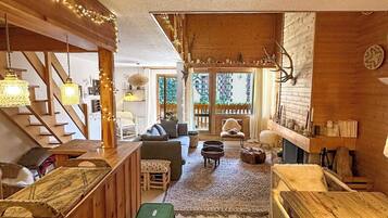 A cozy, rustic interior with wooden beams, a staircase, a bar area, and a seating space with a view of the outdoors.