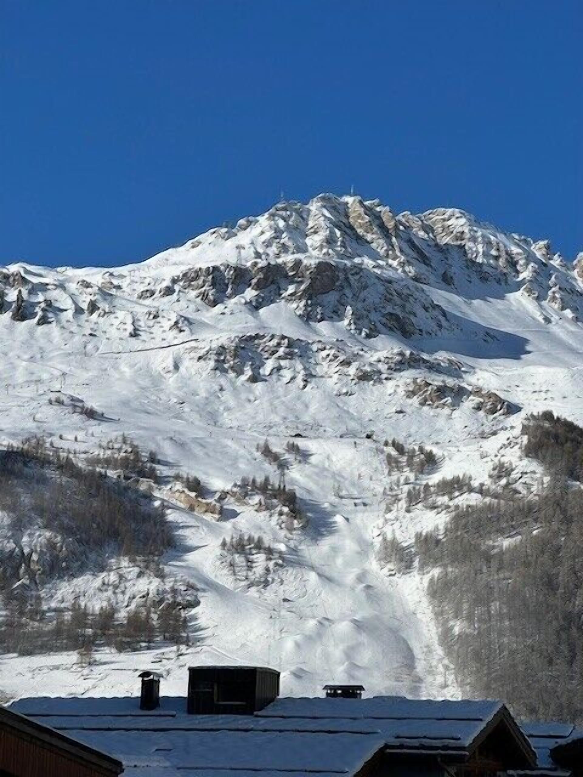 Une montagne dont les pentes sont recouvertes de neige, avec quelques bâtiments à son pied.