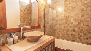Un baño con tocador de madera, un lavabo grande, un espejo y una zona de ducha con paredes de azulejos.