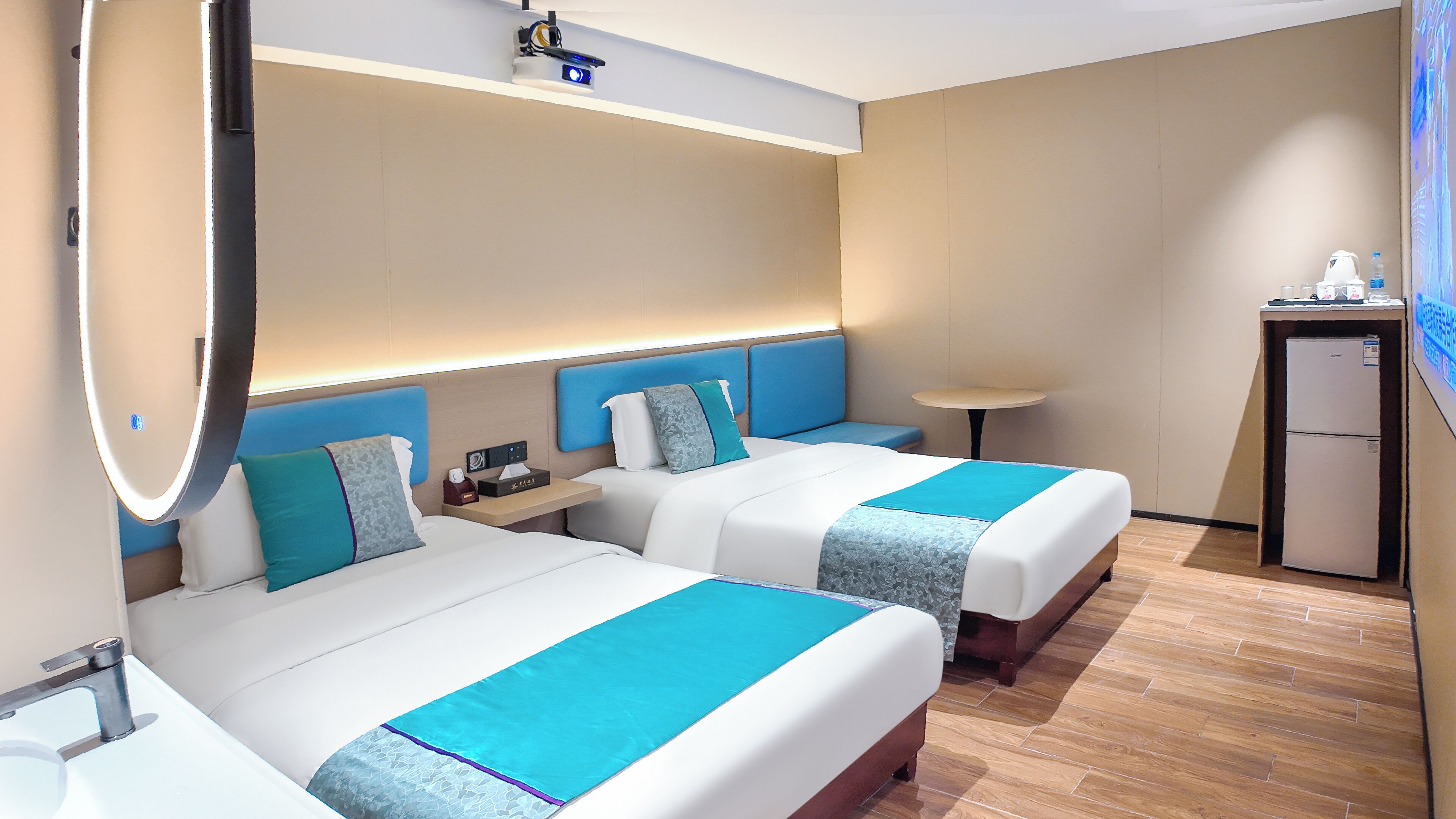 Ein Hotelzimmer mit zwei Betten, einem Schreibtisch, einem kleinen Kühlschrank und einem Fernseher.