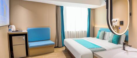 A hotel room with a bed, a desk, a mini-fridge, a mirror, and a sink.
