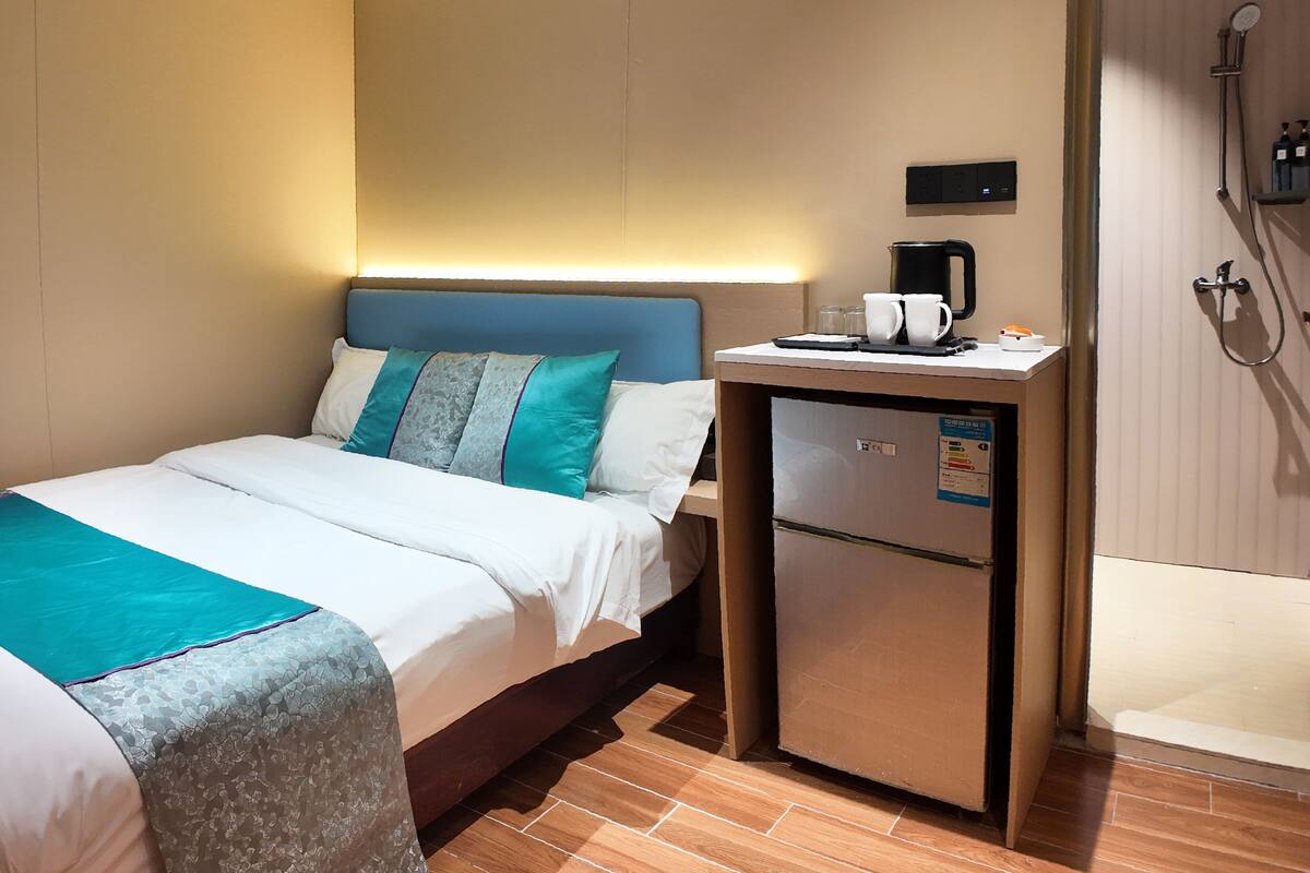 A hotel room with a bed, a small desk with a coffee maker, and a shower area.