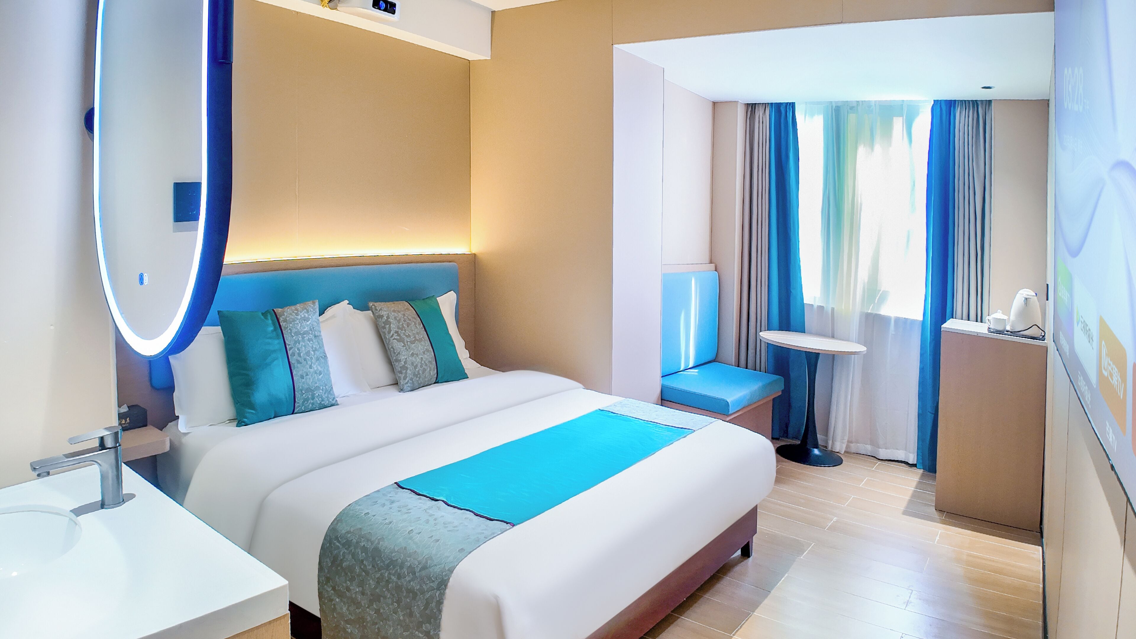 A modern hotel room with a large bed, bedside table, and a small desk with a chair.