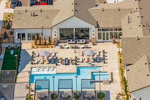 Luftaufnahme eines Hotels mit Schwimmbad, Außenbereich mit Sitzgelegenheiten und einem großen Gebäude mit Glasfassade.