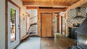 A wooden interior with a staircase, a kitchen area with a stove, and a door leading to an outdoor deck.
