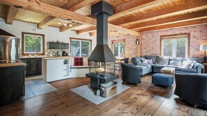 A spacious living area with a fireplace, wooden ceiling beams, and a brick wall.