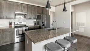A modern kitchen with stainless steel appliances, granite countertops, and bar stools. - Landing | Chic 1BD in Eastpoint (Baytown)