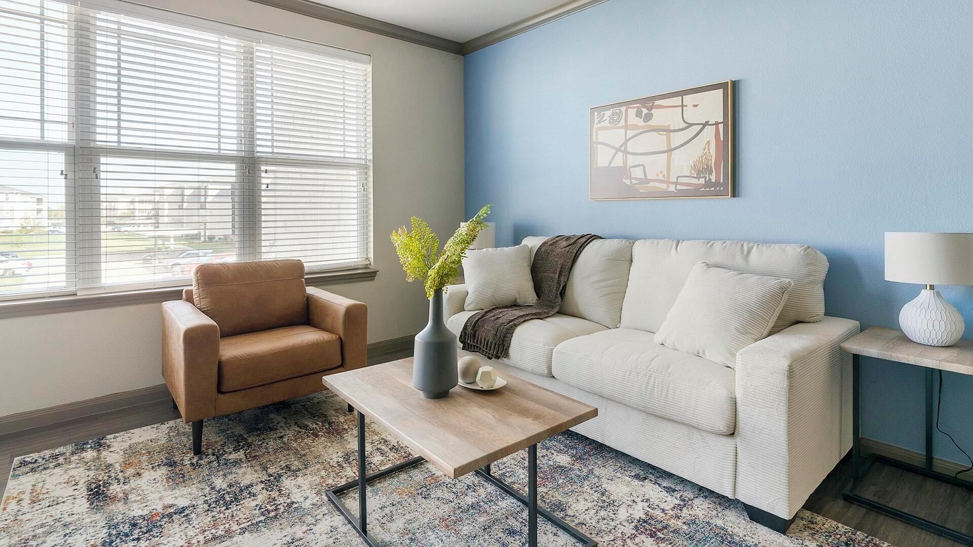 Een woonkamer met een beige bank, een bruine fauteuil, een salontafel en een blauwe accentmuur.