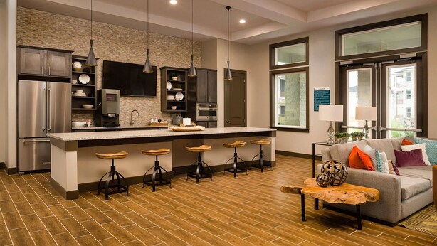 A modern kitchen with a central island, bar stools, and a dining area with a sofa and coffee table. - Landing | Chic 2BD in Eastpoint (Baytown)