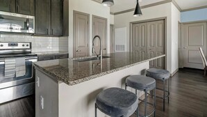 A modern kitchen with granite countertops, stainless steel appliances, and a bar area with stools. - Landing | Chic 2BD in Eastpoint (Baytown)