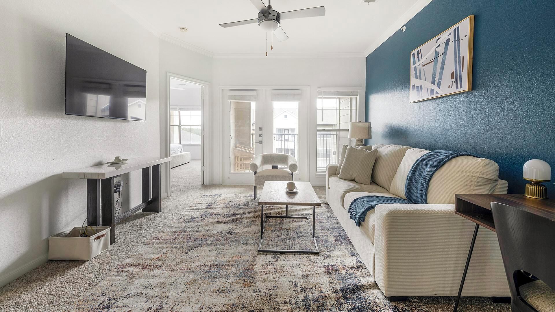 A spacious living room with a large TV, a sofa, a coffee table, and a blue accent wall.