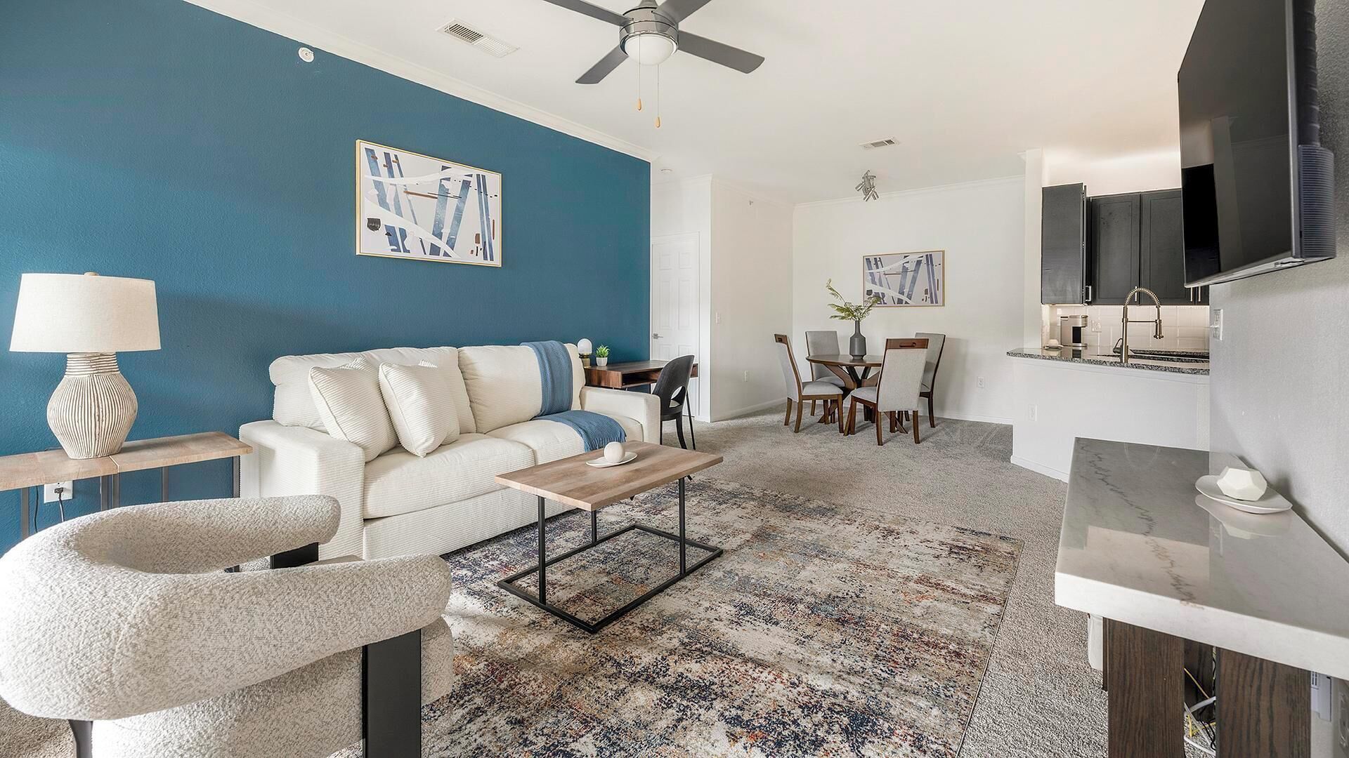 Un salon moderne avec un mur d’accent bleu, un canapé blanc, une table basse et un coin repas comprenant des chaises et une table.