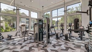 Un gimnasio con diverso equipo de ejercicio, amplias ventanas y suelo estampado.