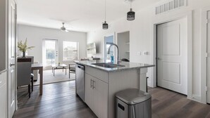 Cozinha moderna com ilha central, área de jantar com mesa e cadeiras, e vista para a cidade através de grandes janelas.