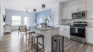 A modern kitchen with a central island, stainless steel appliances, and a bar stool seating area. - Landing | Modern 1BD, Gym, Pool (Leander)