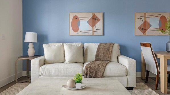 Ein Wohnzimmer mit einer Couch, einem Couchtisch, einer Lampe und zwei abstrakten Bildern an der Wand.