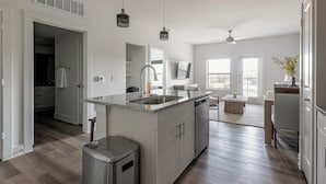 Uma cozinha moderna com uma ilha central, eletrodomésticos de aço inoxidável e vista para a sala de estar.