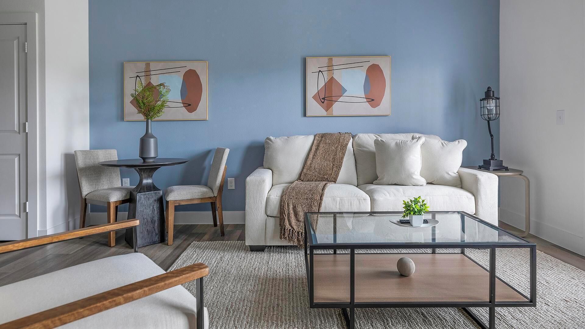Ein Wohnzimmer mit einem weißen Sofa, zwei Sesseln, einem Couchtisch und zwei abstrakten Bildern an der Wand.