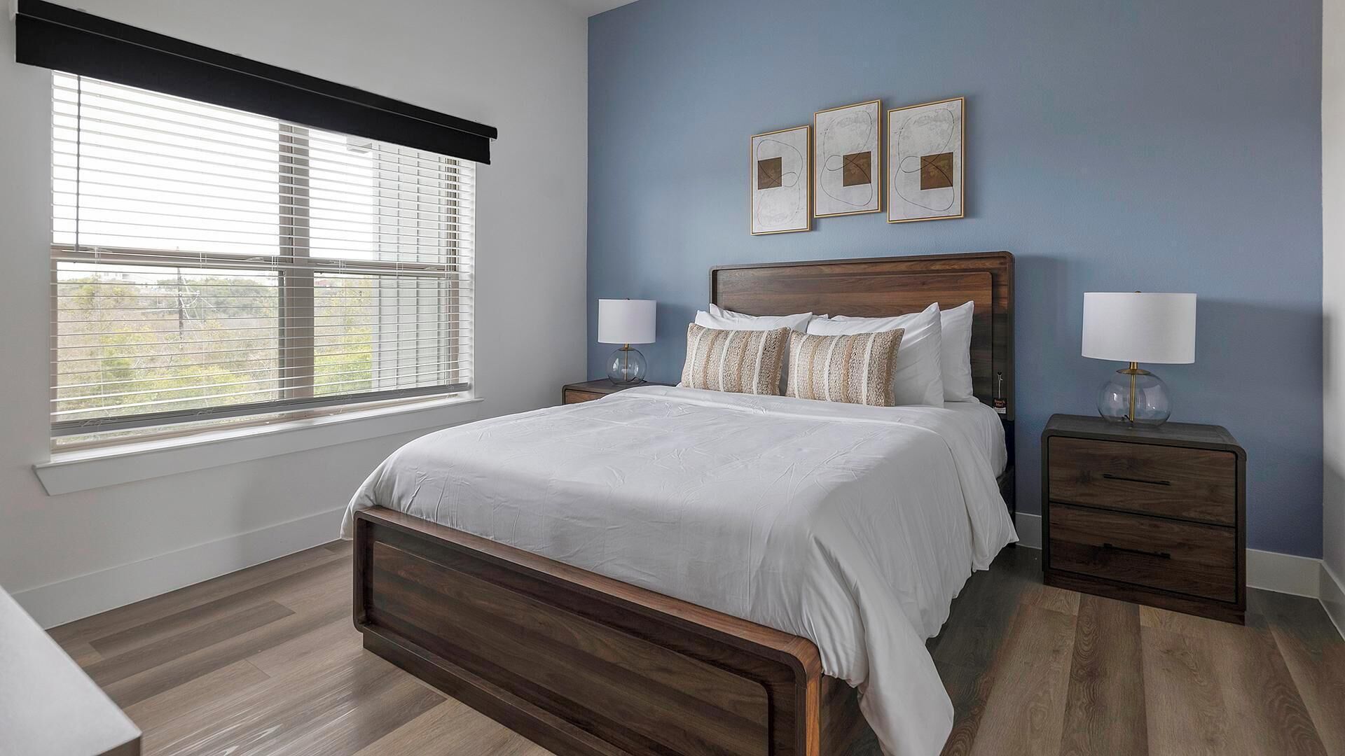 Een slaapkamer met een houten bed, twee nachtkastjes, een raam met zonwering en drie ingekaderde foto's aan de muur.