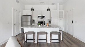 A modern kitchen with a central island, stainless steel appliances, and bar stools. - Landing | Stylish 2BD, Gym, Pool (Leander)