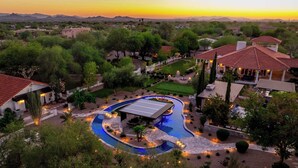 Un resort lujoso con una gran piscina, jardines ajardinados y varios edificios con techos de tejas rojas.