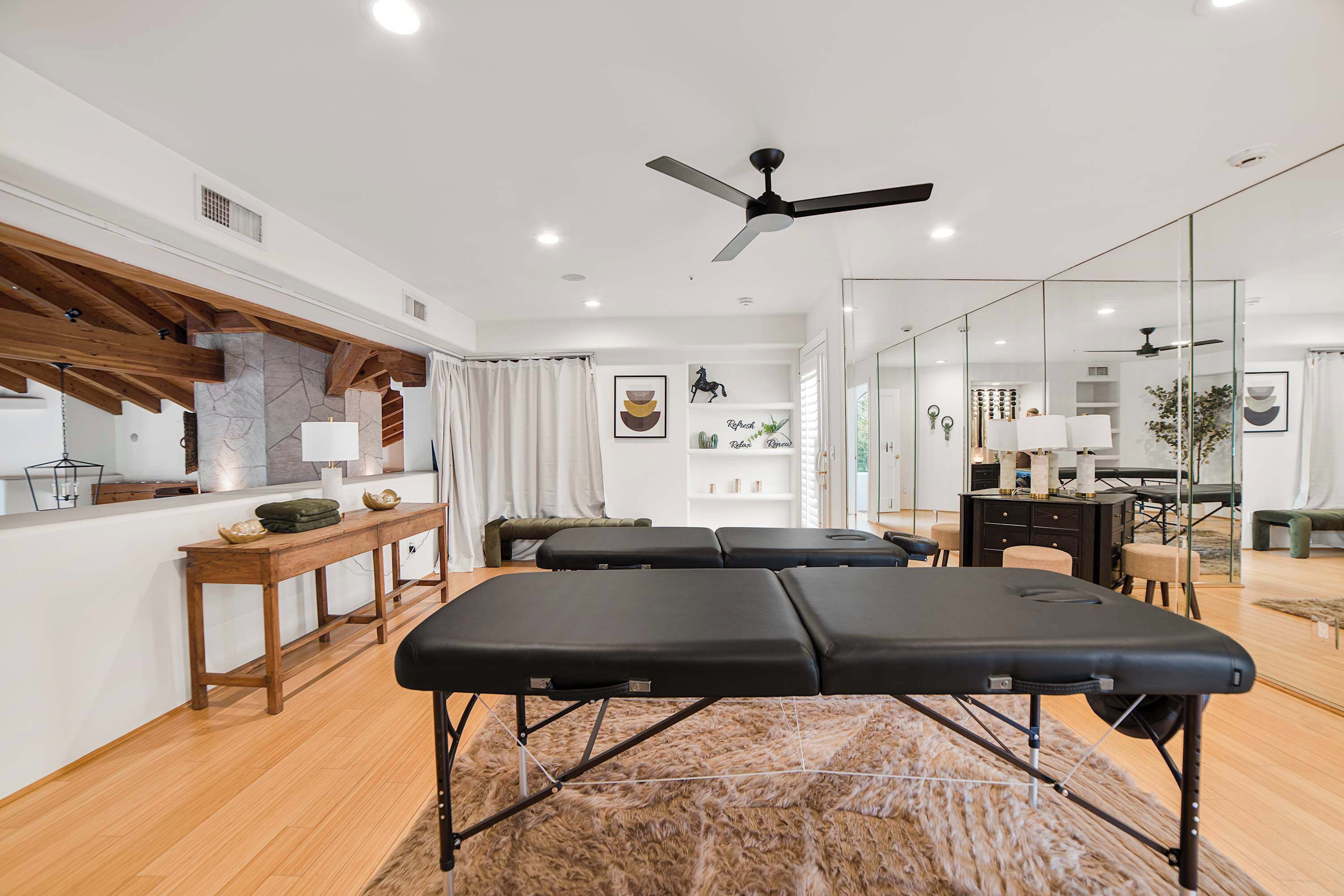 A modern spa room with wooden beams, a massage table, a reception desk, and a mirror wall.