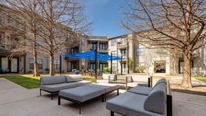 A courtyard with outdoor seating, a blue umbrella, and a building with multiple windows and balconies. - Landing | Spectacular 1BD, Gym, Courtyard (Austin)