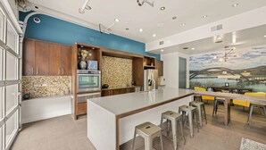 A modern kitchen with a central island, bar stools, and a mural of a bridge over water. - Landing | Spectacular 1BD, Gym, Courtyard (Austin)