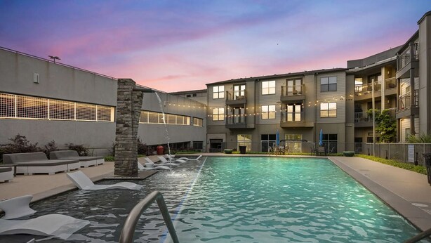 A pool area with a stone feature, lounge seating, and a multi-story building with balconies. - Landing | Spectacular 1BD, Gym, Courtyard (Austin)