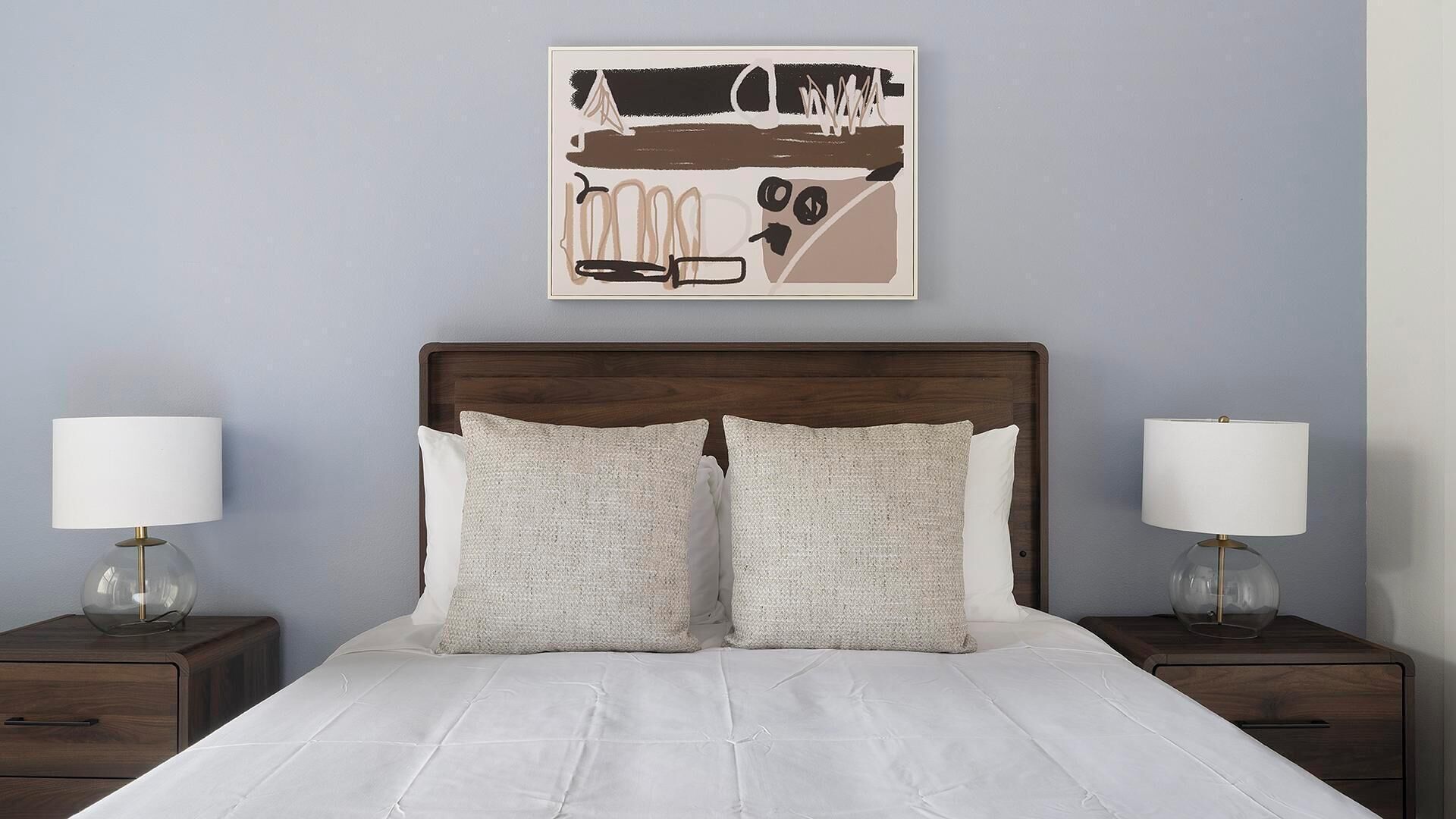 Un lit bien fait, avec deux oreillers, une tête de lit en bois et deux tables de chevet avec des lampes.