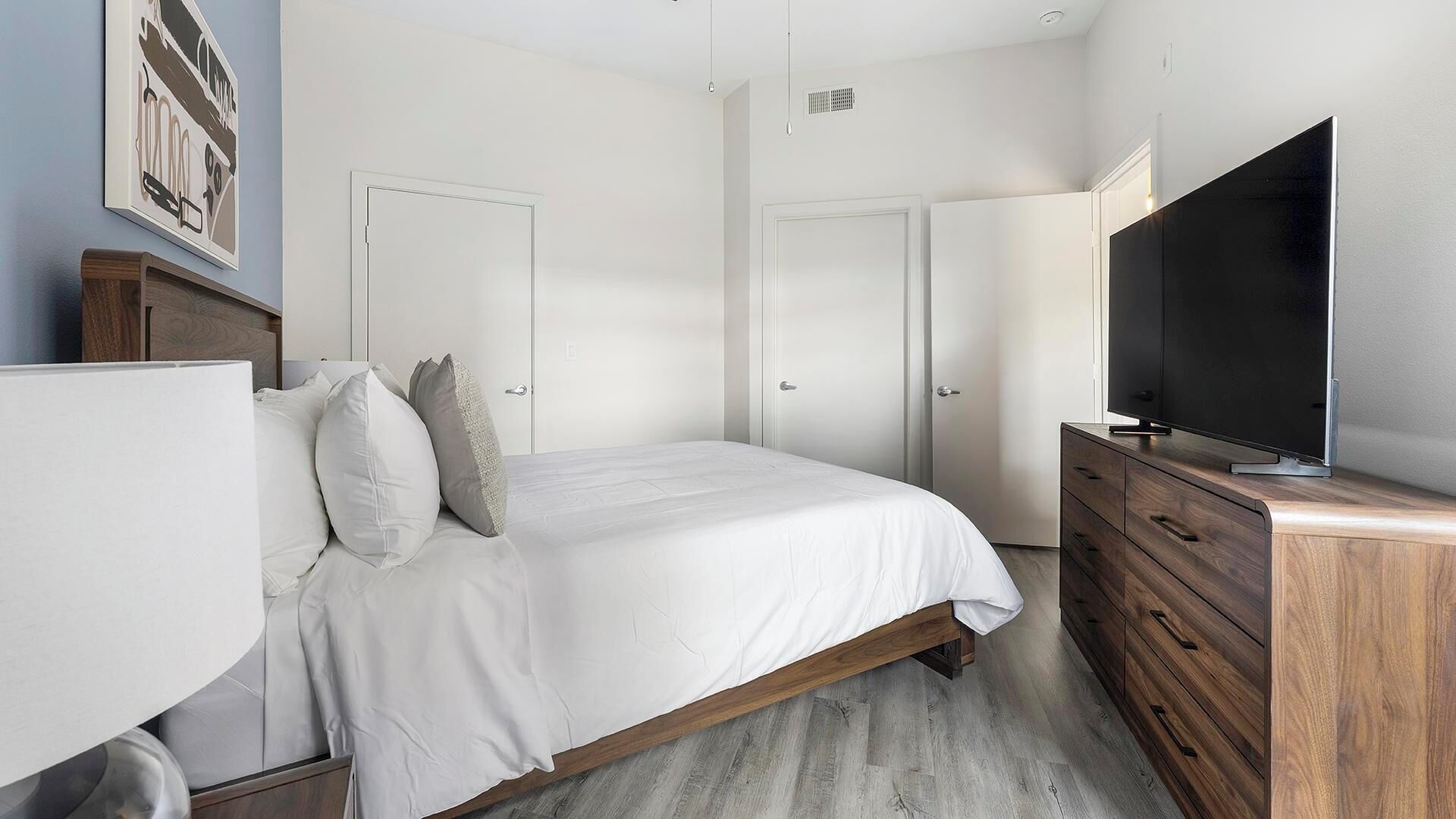 A bedroom with a bed, a dresser, a TV, and two doors.