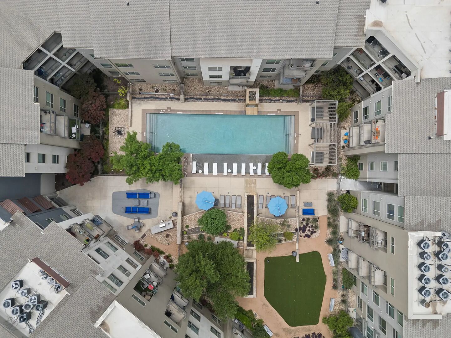 Vista aèria d'un hotel amb una piscina central, zones d'estar a l'aire lliure i un jardí petit.