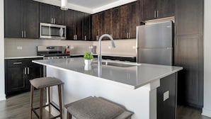 Een moderne keuken met donkerhouten kastjes, roestvrijstalen apparatuur, een centraal eiland met krukken en een inbouwmagnetron.