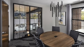 Een vergaderruimte met een ronde tafel, zwarte stoelen, een groot raam met uitzicht en een moderne hanglamp.
