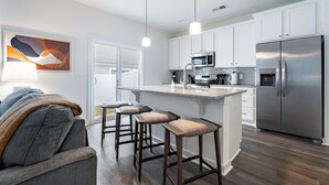 A modern kitchen with white cabinets, stainless steel appliances, and a bar area with stools. - Landing | Stunning 1BD, Pool, Gym (Port Wentworth)