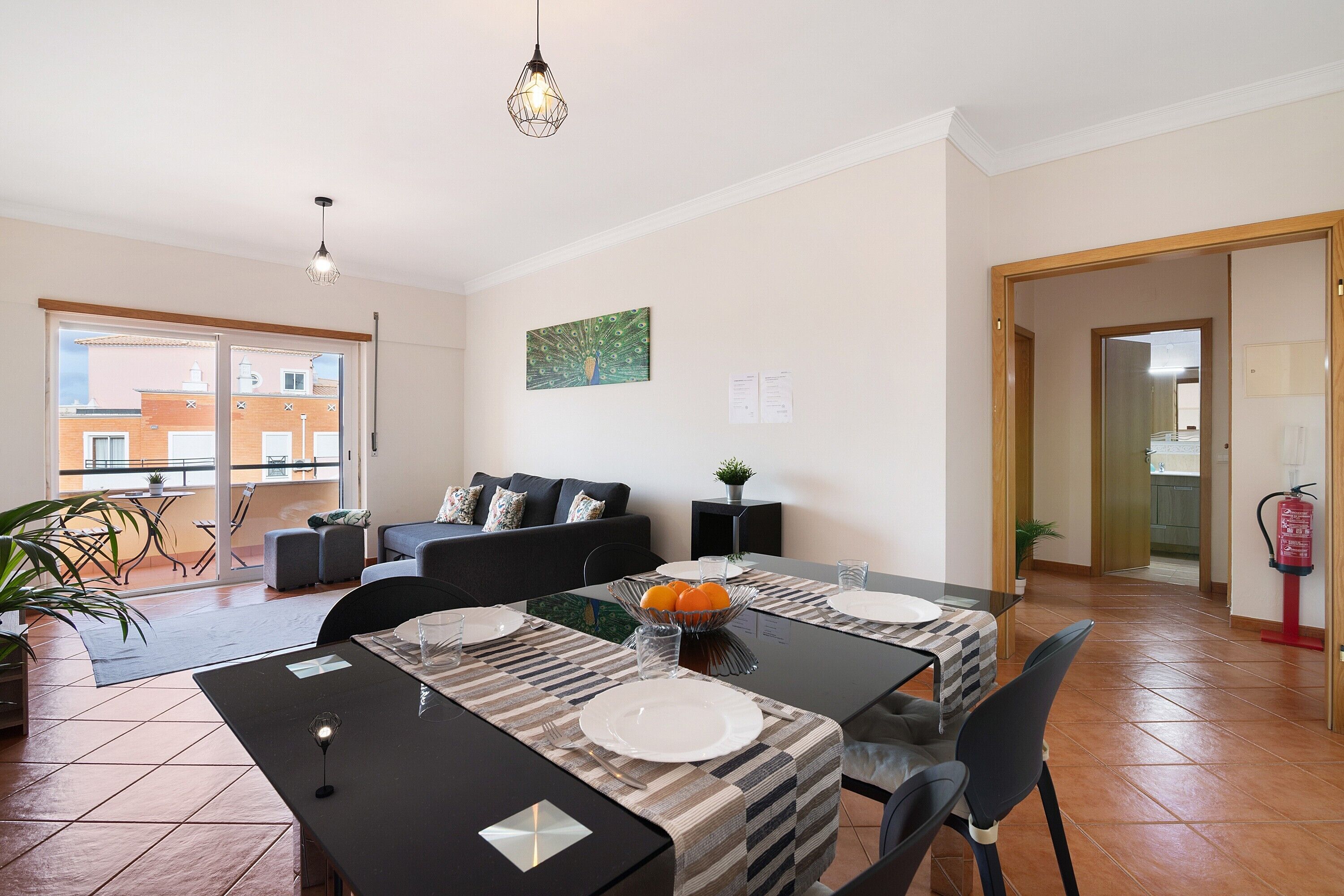 Espaço de refeições com mesa posta para quatro pessoas, um sofá e vista para edifícios.