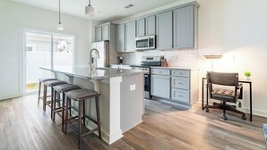 A modern kitchen with grey cabinets, a central island with bar stools, a microwave, and a stove.