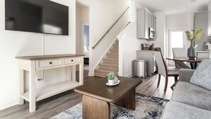 A modern living room with a flat-screen TV, a wooden coffee table, a sofa, and a staircase leading to a kitchen area. - Landing | Spectacular 3BD, Clubhouse, Pool (Port Wentworth)