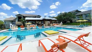 Una piscina con sillas de descanso y sombrillas, rodeada de edificios con tejados de piedra y metal.