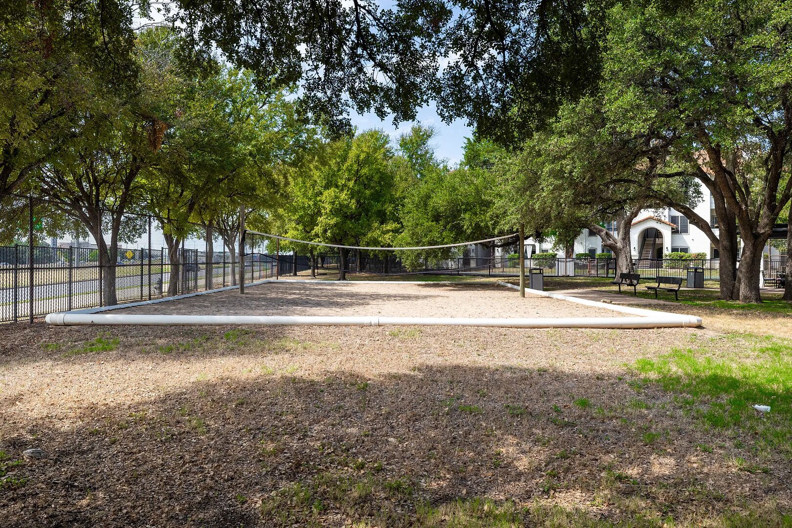 A volleyball court with a net, surrounded by trees and a fence.