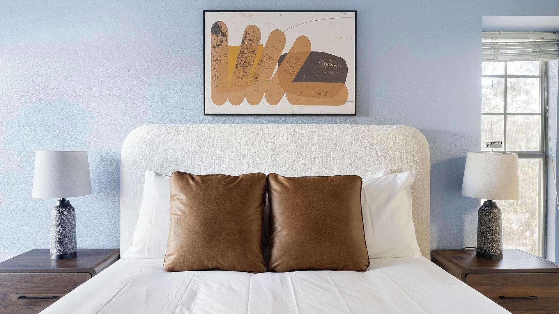 A neatly made bed with white and brown pillows, a textured headboard, and two bedside lamps on wooden nightstands.