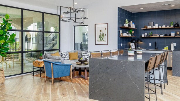 Eine moderne Küche mit einer großen Kochinsel, Barhocker und einem Essbereich mit einer Couch und Sesseln.